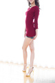 Adjusting hem of scarlet dress legs crossed in high heels